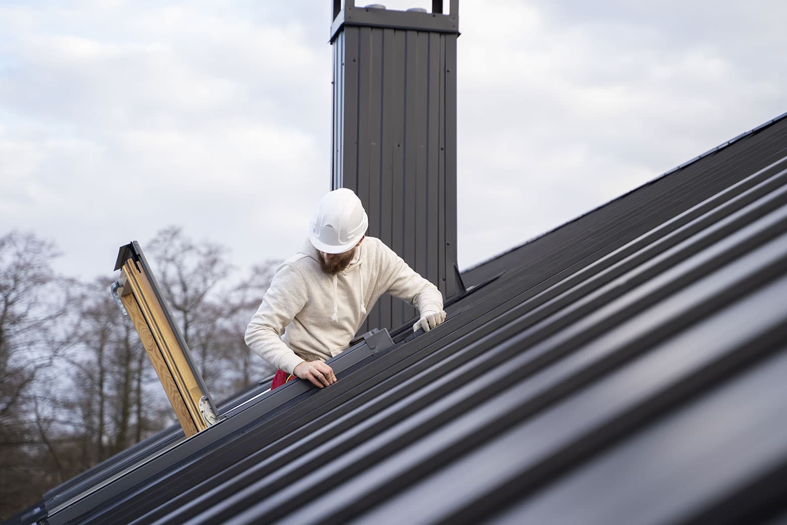 Roofer detailing a wood stove chimney pipe and skylight flashing on a metal roof