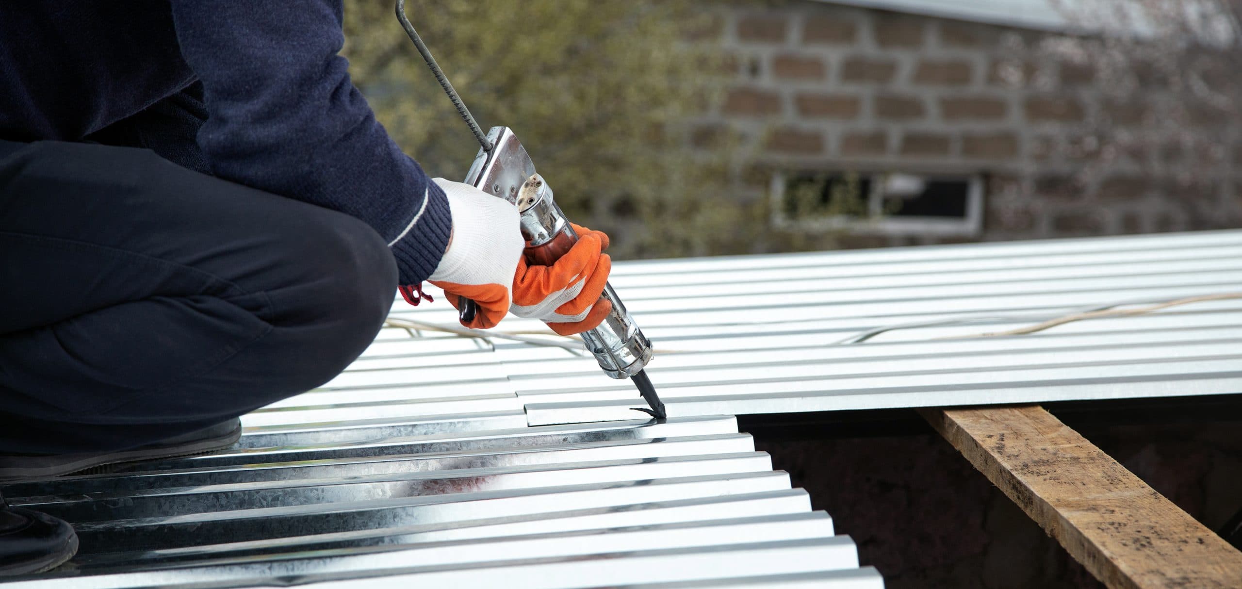 Contractor fastening heavy-gauge corrugated metal roofing panels with a rivet gun